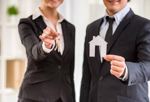 two real estate agents holding keys and house