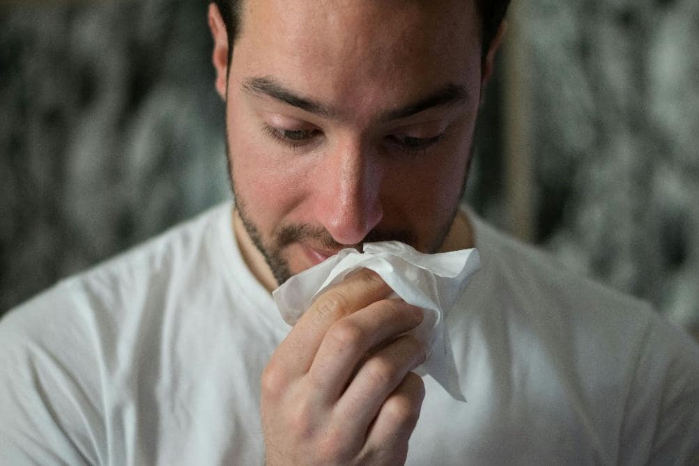 Man holding a tissue to his nose, representing sinus infection symptoms such as congestion, runny nose, and facial irritation.