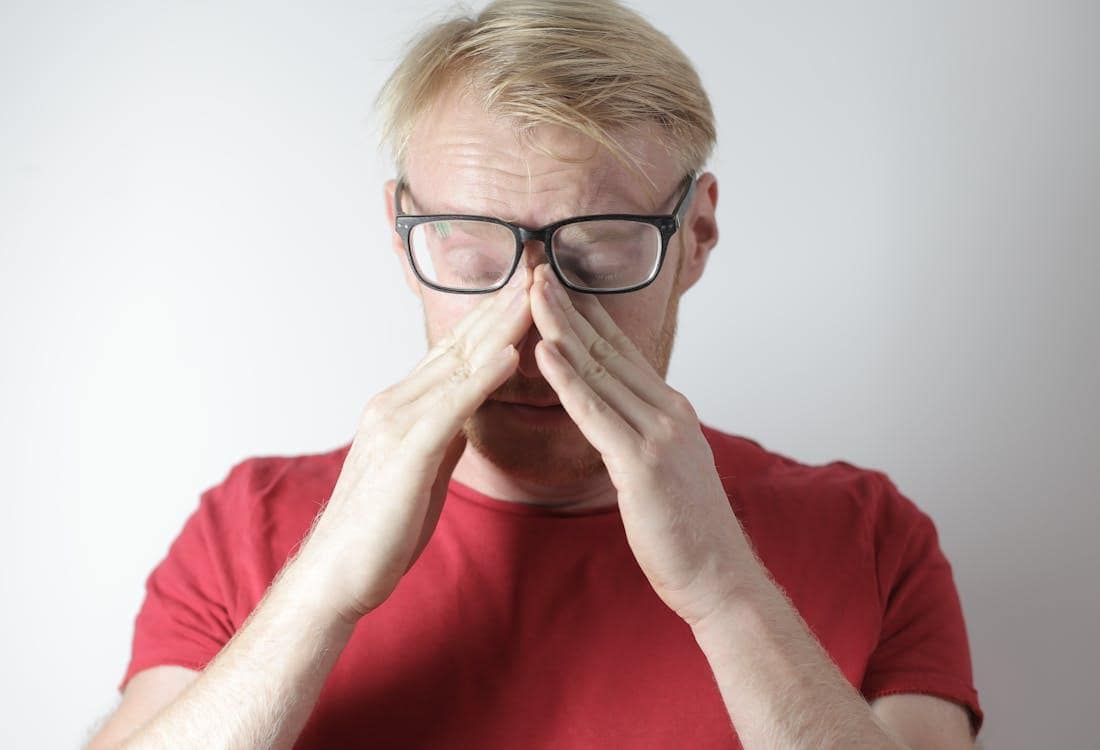 Man with glasses experiencing sinus pressure and facial pain, holding the bridge of his nose