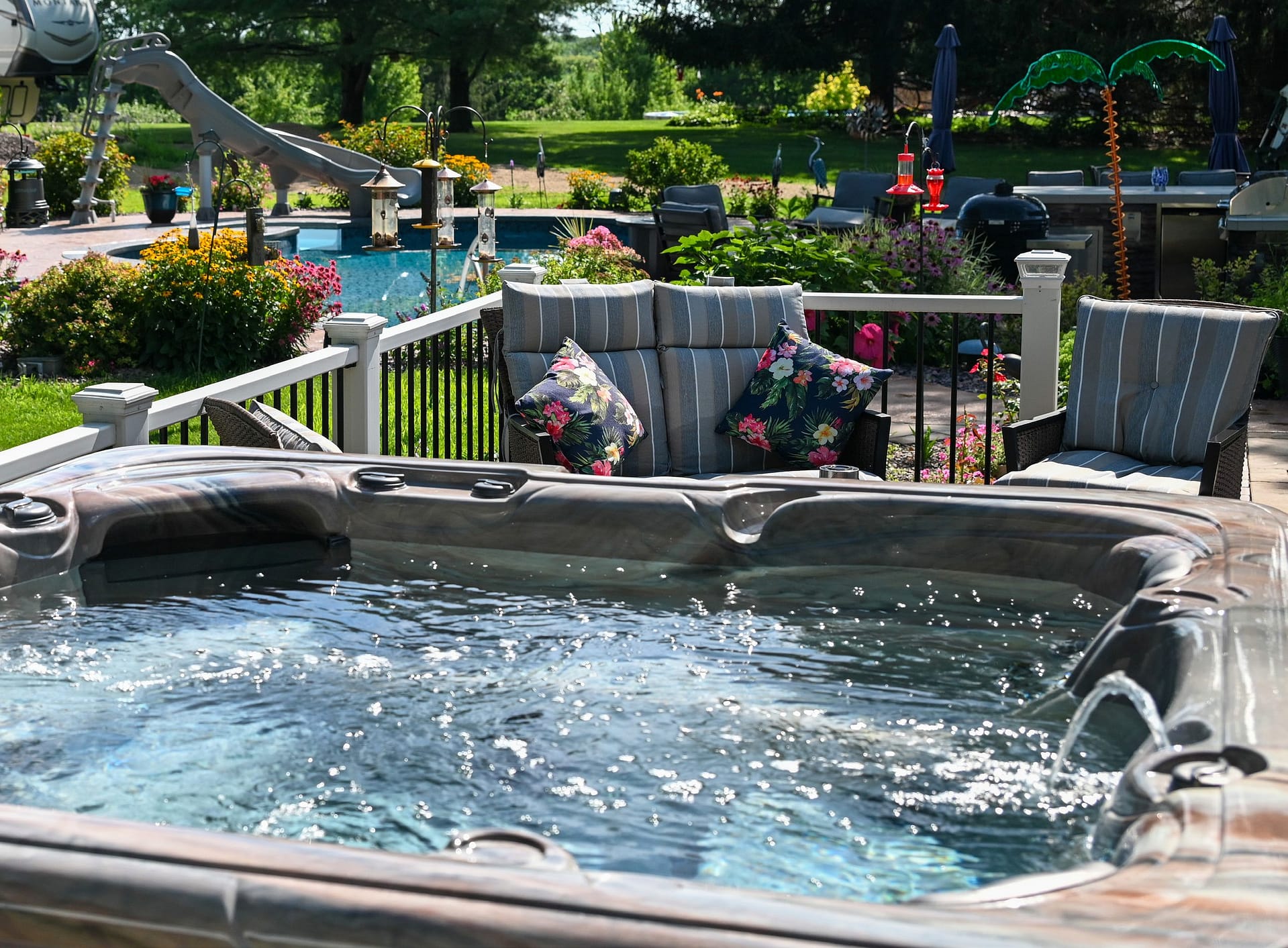 A Garden Leisure hot tub on a patio in a landscaped backyard, with a pool and seating beyond