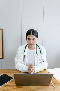 Healthcare provider seated at a desk using a laptop during an online doctor consultation.