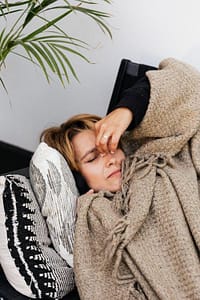 Woman resting under a blanket with her hand on her head, feeling fatigue from a sinus infection
