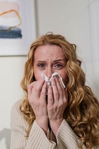 Woman with watery eyes and a runny nose using a tissue due to sinus infection symptoms