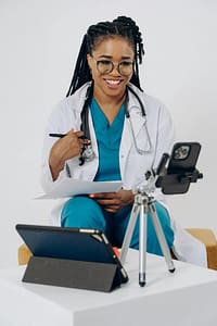 Patient holding medication during a video telehealth appointment with a healthcare provider on a laptop screen.