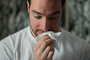 Man holding a tissue to his nose, representing sinus infection symptoms such as congestion, runny nose, and facial irritation.