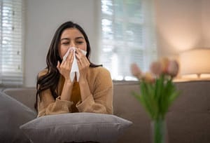 woman blowing nose into tissue in living room