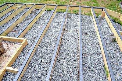 A ground-level deck frame constructed with pressure-treated lumber, sitting on concrete blocks with a gravel base underneath.