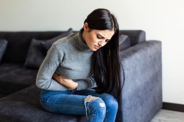 A woman experiencing abdominal pain while resting on a couch.
