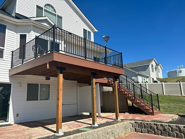 Picture a brown PVC deck paired with a sleek black modern handrail, resting securely on substantial concrete footings. The staircase boasts mid-span support for robust stability, while its steps are elegantly wrapped in LP SmartSide, enhancing its visual appeal.