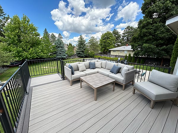 Freshly built composite TimberTech deck with Fortress handrail, featuring new L-shaped outdoor furniture, green grass, and blue sky with clouds.