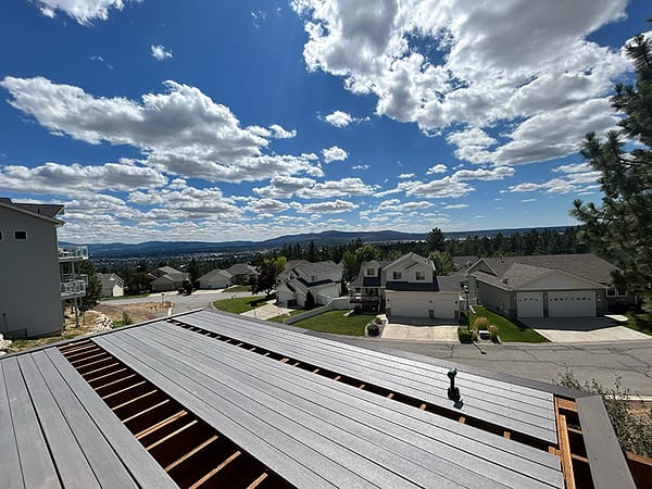 Deck boards being installed on a picture-framed deck overlooking the city, with blue skies, clouds, and sunlight.