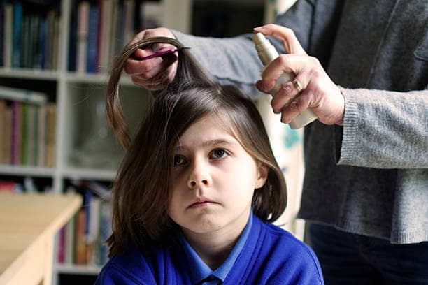 A mother spraying her daughter's hair with head lice treatment