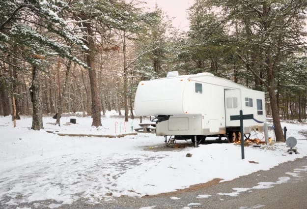 Fifth-wheel travel trailer at a snow-covered wooded campsite in winter