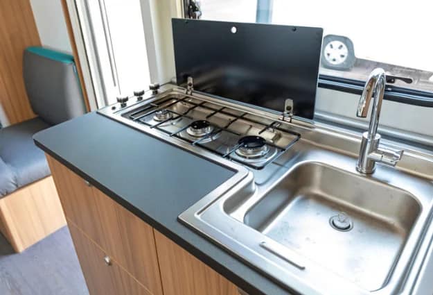Compact RV kitchen with a stainless steel sink, faucet, and gas stove