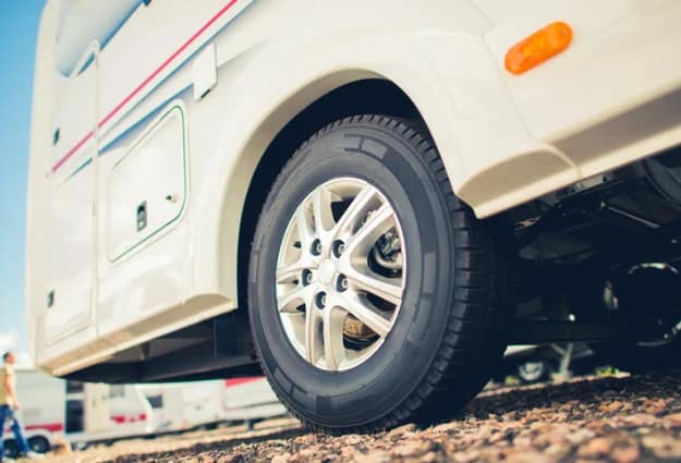 Close-up of an RV tire and wheel on a gravel lot