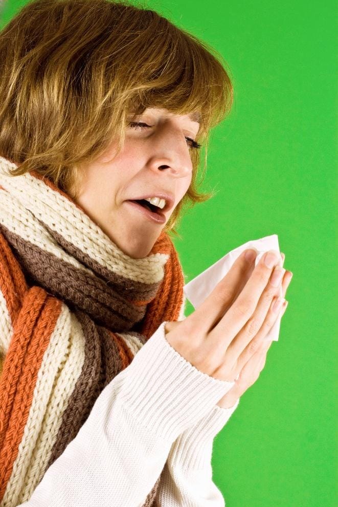 Woman wearing a scarf holding a tissue while sneezing.