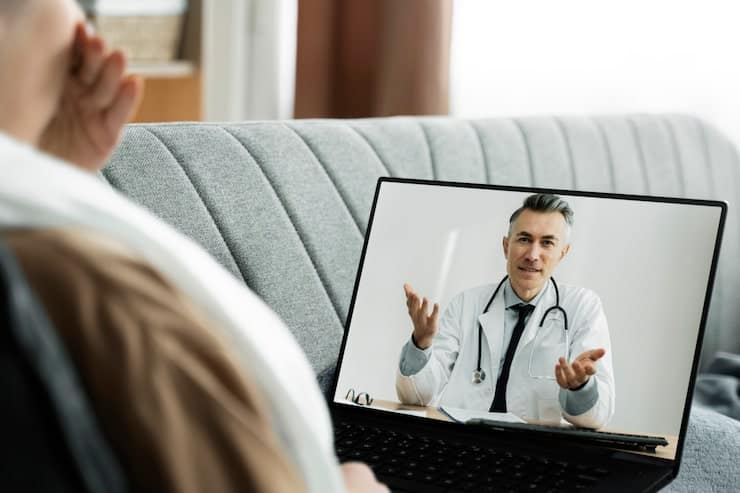 A doctor speaking with a patient through a video consultation on a laptop screen.