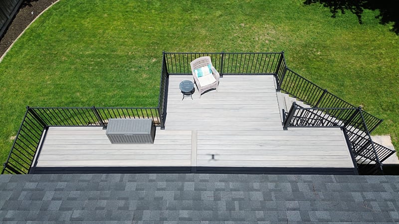 A bird's-eye view of a second-story deck with a bump-out, nestled in a vibrant green backyard.