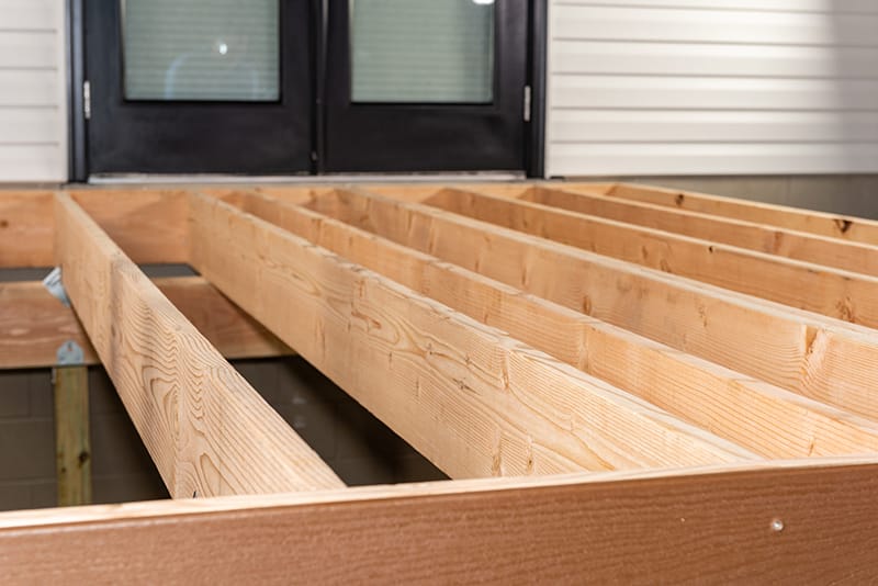 Framed deck using Douglas fir, second-story doors in the background, supported by a beam against a cinder block foundation.