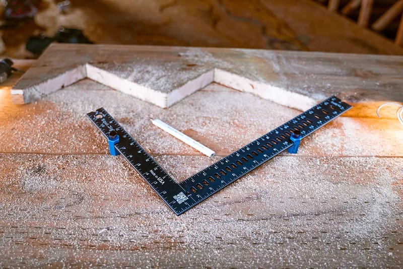 Close-up view of a freshly cut stair stringer with a blue framing square and stair gauges placed on it.