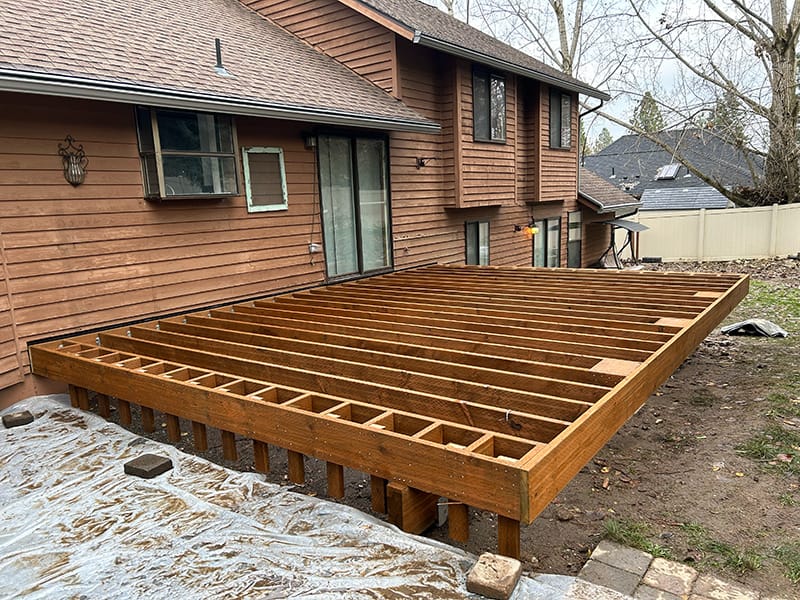 Side view of a freshly framed pressure-treated deck on a sloped yard in Spokane, Washington, with special step framing on the left side.