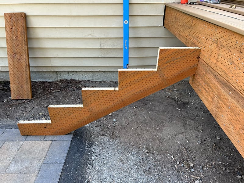 Pressure-treated stair stringer positioned on a deck with its bottom landing on a paver patio, showing setup for the landing and deck attachment.