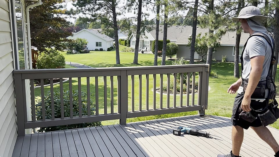 A professional deck builder walking from right to left, preparing to grab a sawzall to cut and remove the handrail during a deck demolition project.