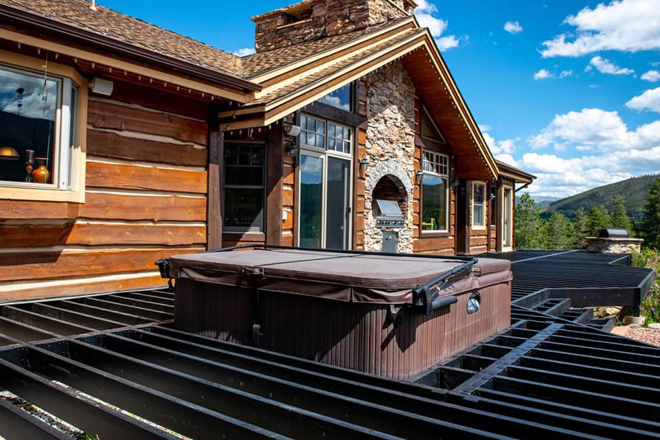 Deck framed with Fortress Evolution steel framing, featuring a built-in hot tub, with a view of a home, green trees, and blue sky in Spokane, Washington.