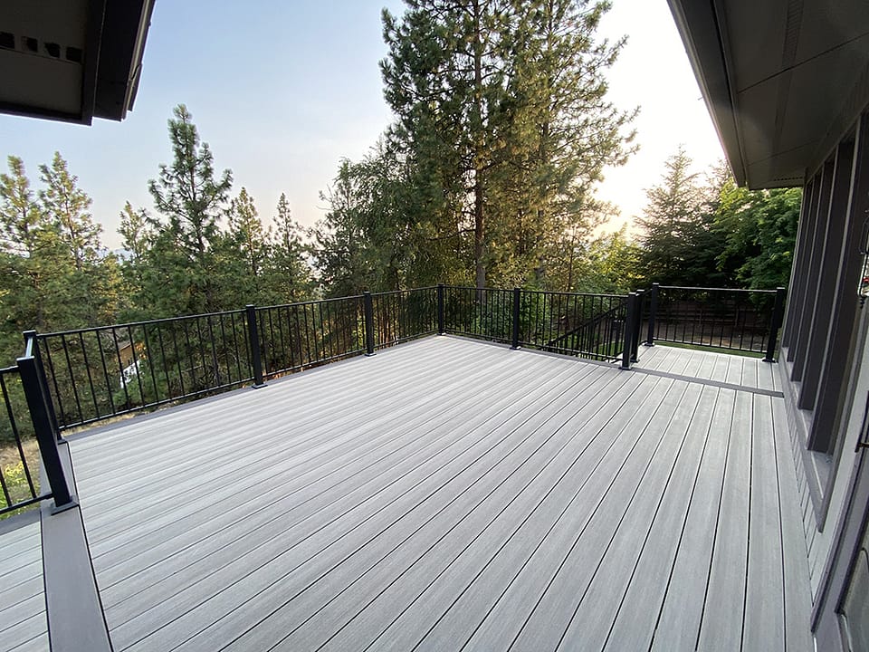 Large custom deck off the back of a house with a backdrop of tall pine trees.