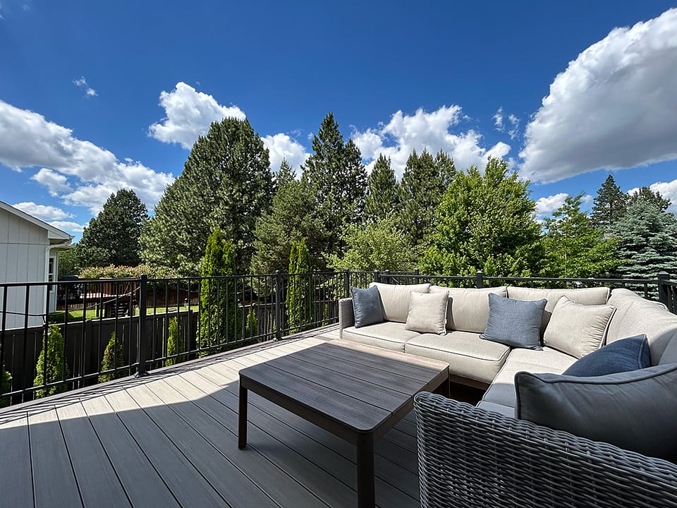 Beautiful deck with L-shaped furniture and a coffee table, overlooking a serene backyard.