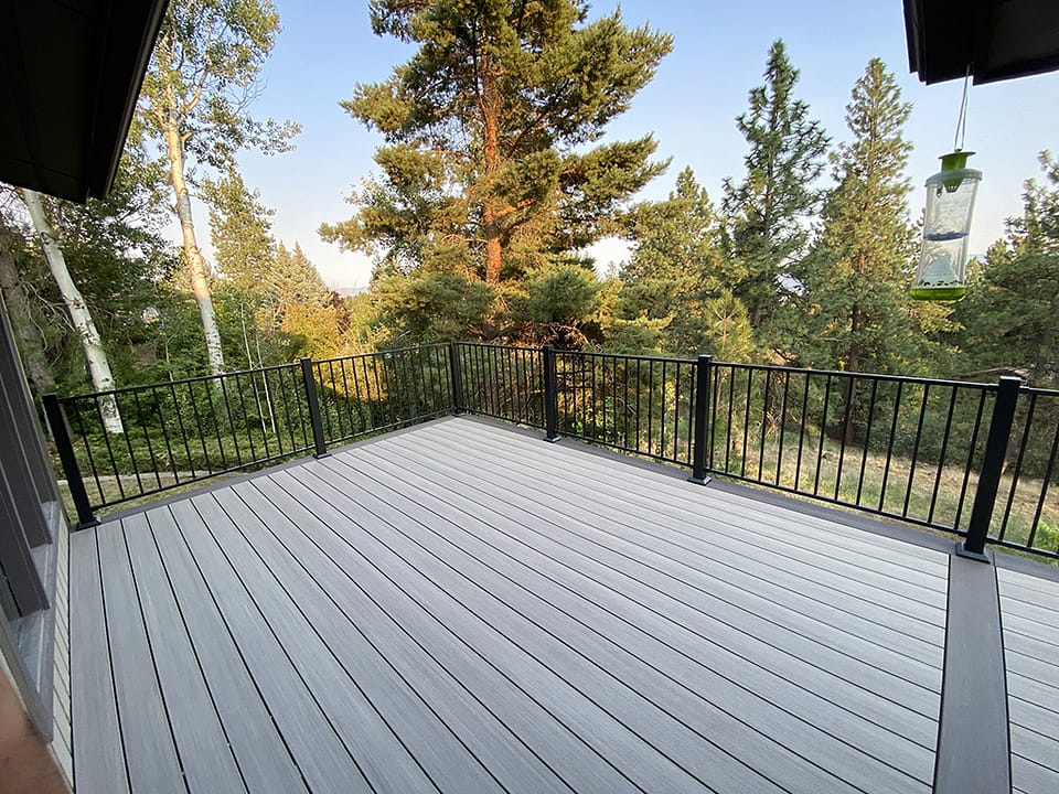 Large section of a back deck on a home with a pine tree backdrop and wide border decking.