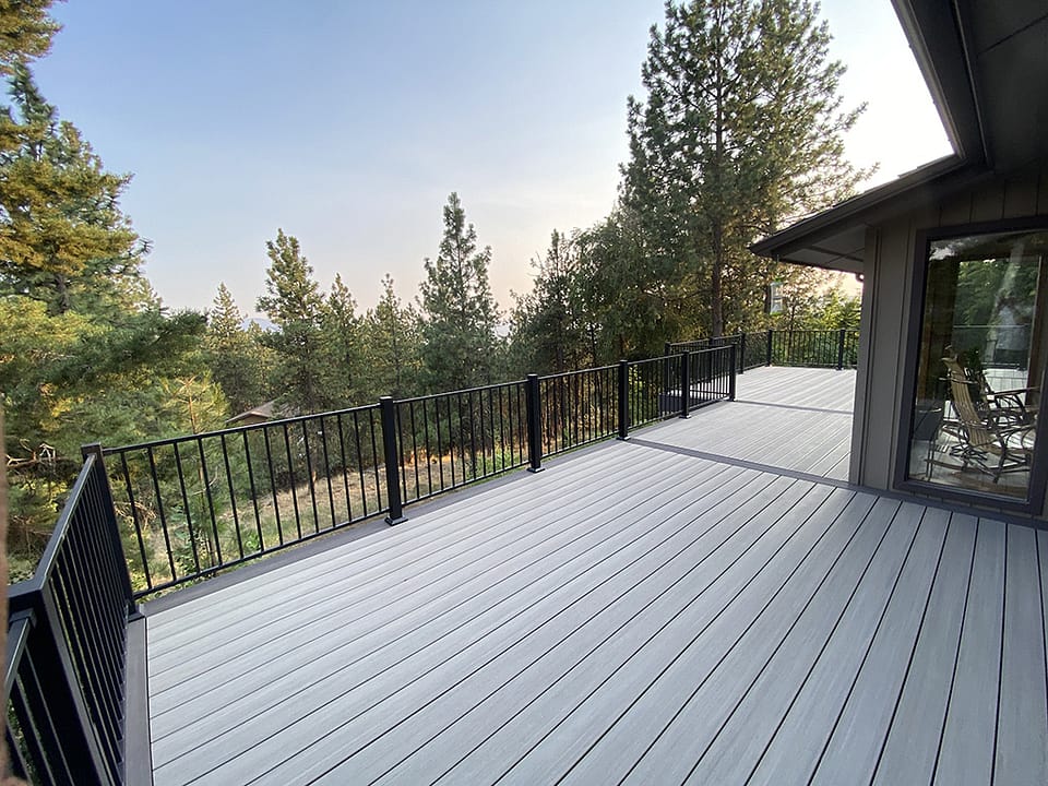 Large custom deck spanning the back of a home with three connected sections and a backdrop of tall pine trees.