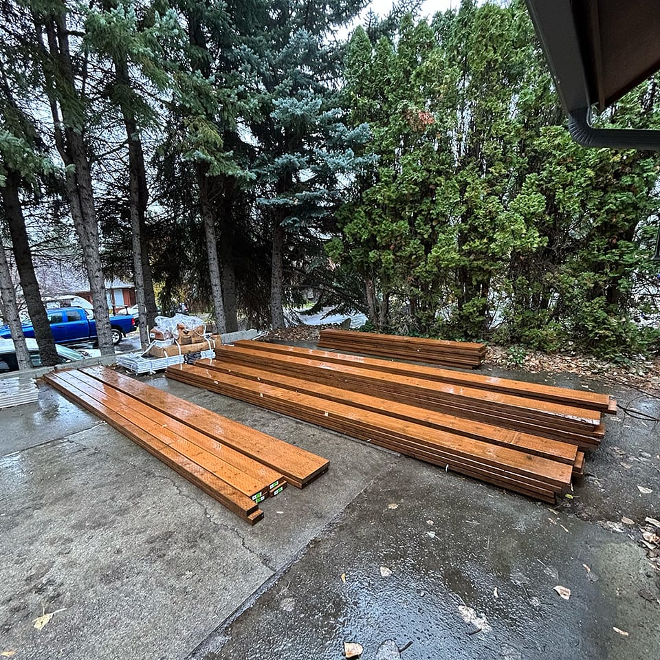 Pressure-treated wood framing laying on wet ground in Spokane, Washington, organized for deck construction after recent rainfall.