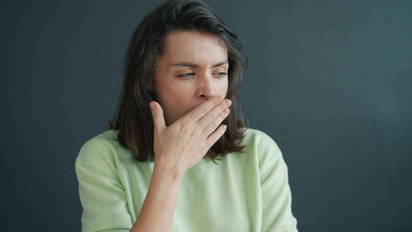 Woman covering her mouth while appearing tired, representing fatigue, cough, or cold and allergy symptoms.