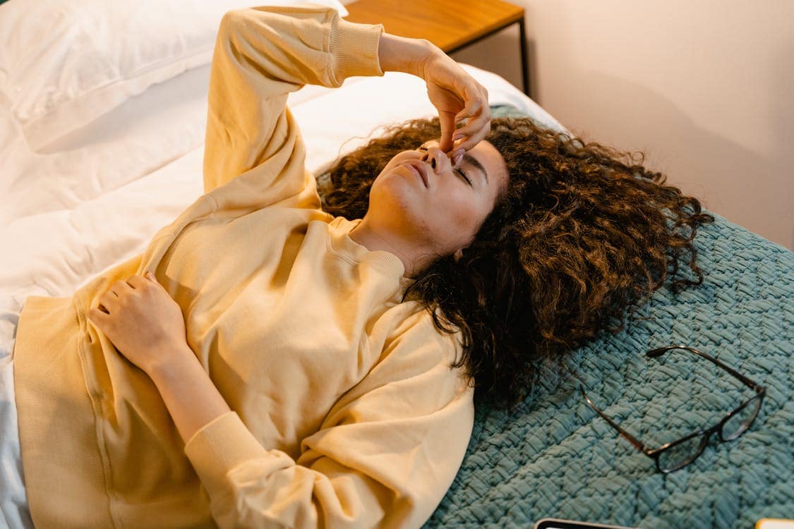 Woman lying on bed holding forehead between eyebrows due to sinus headache