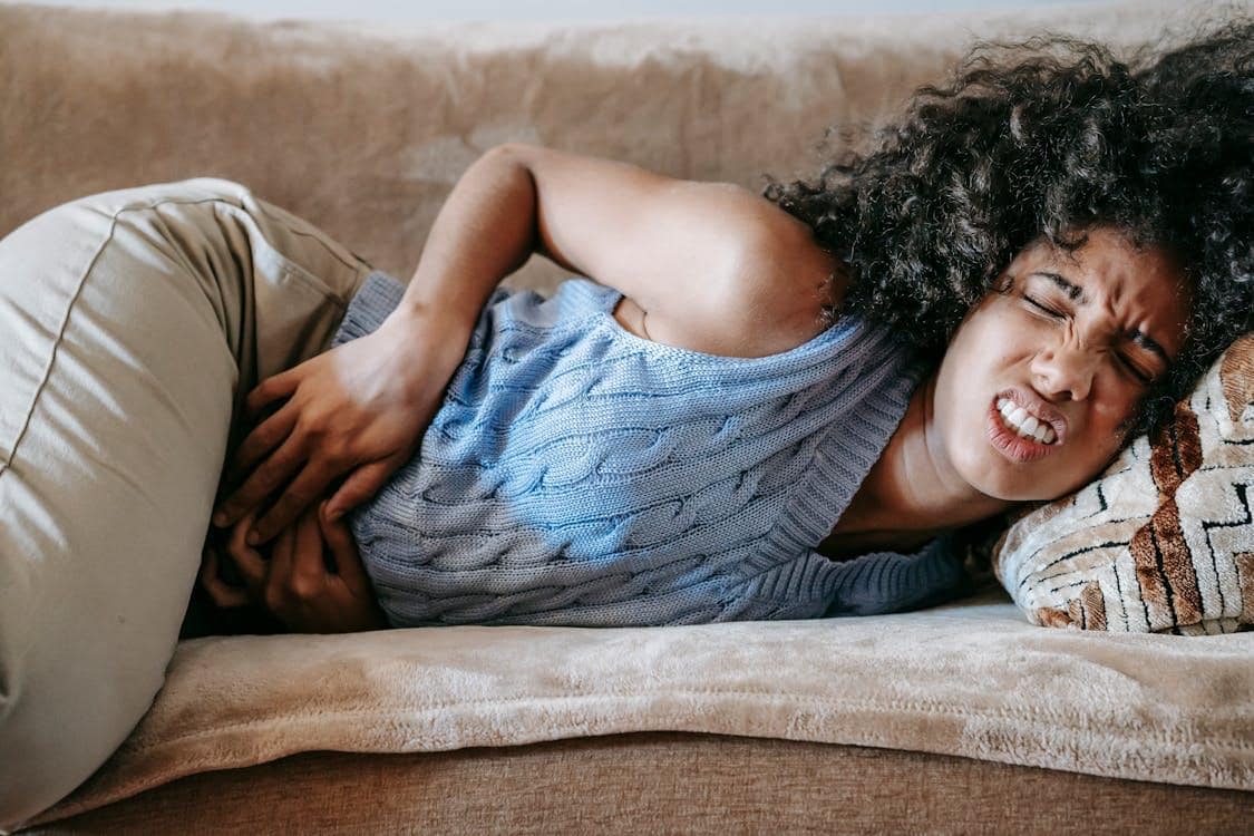 Woman lying down with eyes closed and hands on abdomen showing intense discomfort from UTI symptoms