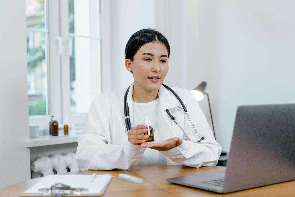 Healthcare provider speaking with a patient on a laptop while discussing medication during a virtual doctor appointment.