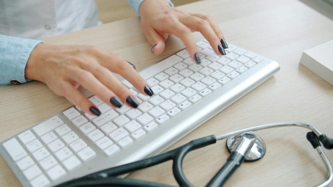 Hands typing on a keyboard beside a stethoscope.