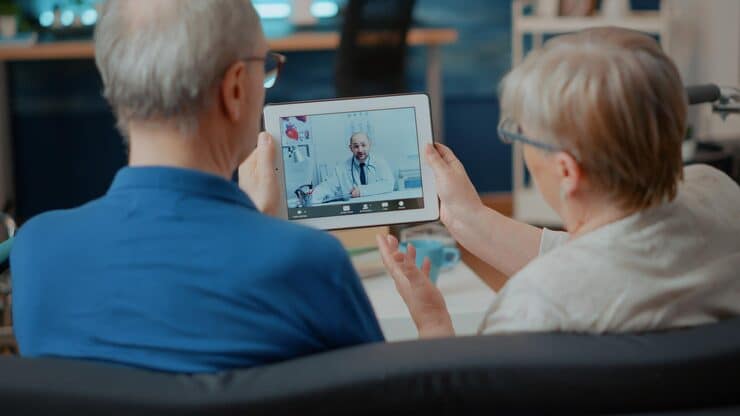 An elderly couple speaking with a doctor through a telehealth video call on a tablet.