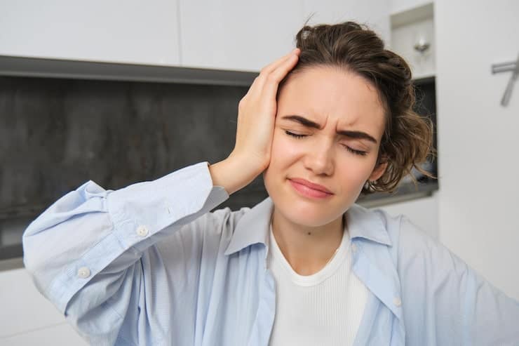 A woman experiencing facial pain and sinus pressure while holding her forehead and cheeks.